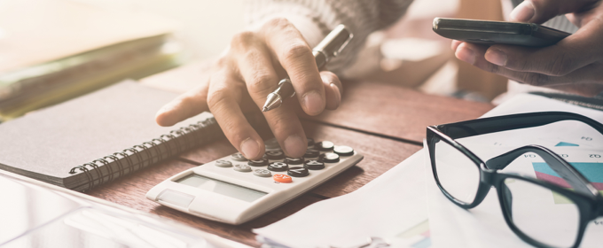 Close-up of hands using a calculator and smartphone at a desk