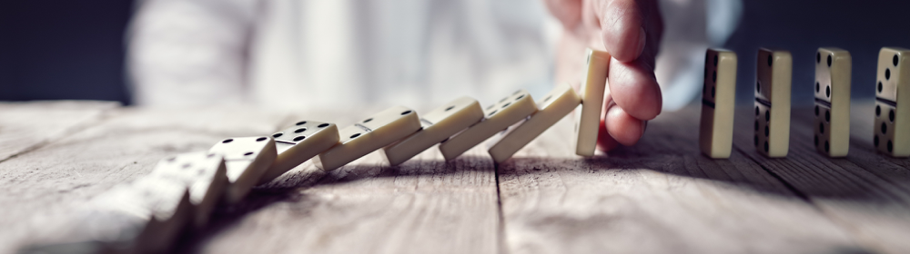 Hand stopping dominoes from falling, representing financial risk